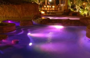 A backyard swimming pool with a hot tub and a paver patio.