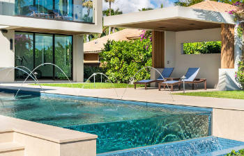 Outdoor armchairs and a table on a wooden deck of a backyard residential swimming pool.