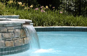 A backyard swimming pool with a hot tub and a paver patio.