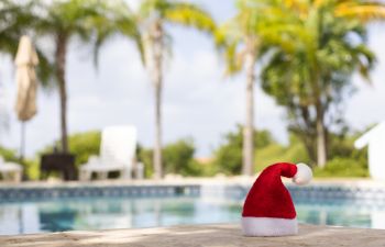 A Christmas hat standing by a swimming pool surrounded with palm trees.