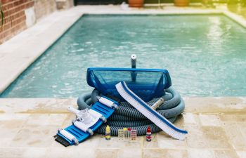 Pool cleaning and maintenance equipment on the edge of a swimming pool deck.