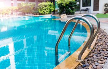 Outdoor armchairs and a table on a wooden deck of a backyard residential swimming pool.