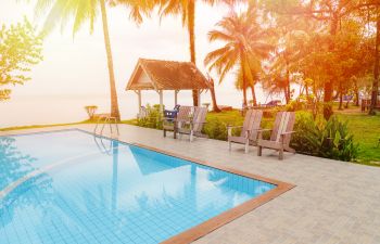 Outdoor armchairs and a table on a wooden deck of a backyard residential swimming pool.