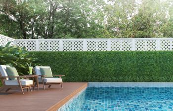 Outdoor armchairs and a table on a wooden deck of a backyard residential swimming pool.